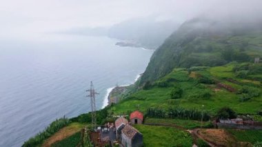 Sisli tepeler ve okyanus manzarası. Küçük bir köy yaz seyahati. Yuvarlanan yamaçları olan insansız hava aracı yeşil dağ sırası. Huzurlu vadi manzaralı manzara ortamı. Küçük, huzurlu evler.