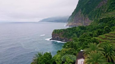 Hava yeşili deniz kıyısı dağları bulutlu bir günde. Karanlık, uçsuz bucaksız okyanus. Muhteşem volkanik tepeler yemyeşil insansız hava aracı görüntüsüyle kaplı. Sisli fırtınalı bir sabahta resimli doğa kıyısı manzarası 