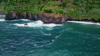Derin okyanus volkanik kıyı manzarasını vuruyor. Soğuk yaz mevsiminde kıyı tepelerinde yemyeşil orman. Fırtınalı bir sabahta karanlık deniz tarafından yıkanan resimli bir pelerin dağı. Dünya üzerinde huzurlu bir yer 