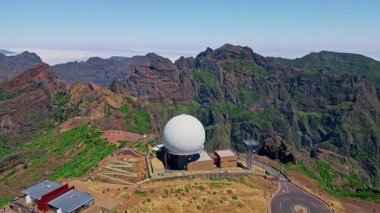 İnsansız hava aracı görüntüsü Madeira adasındaki Pico-do-Arieiro zirvesi. Dağ platosundaki meteorolojik istasyonun beyaz radar kubbesi. Mavi gökyüzünün altındaki görkemli dağlık arazi. Popüler turistik eğlence ve seyahat.