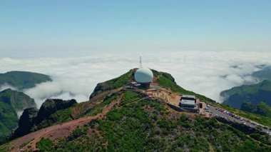 Pico do Arieiro dağındaki büyük beyaz kubbeli meteoroloji istasyonu bulutlarla çevrilidir. Madeira 'nın ünlü cazibesinin güzel panoramik manzarası. Yeşil manzaralı yamaçtaki hava manzaralı yürüyüş alanı.
