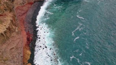 Fırtınalı okyanus taş plaj havadan manzarasını yıkıyor. Kayalık kıyı şeridinde fokurdayan mavi dalgalar. Dalgalı sahil kayalıklarında nefes kesen deniz suyu. Engebeli sahilde güzel bir gel-git.