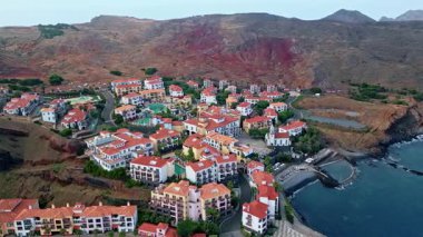 Portekiz kıyı köyünün havadan görünüşü. Yamaçlarda bahçeleri olan güzel kiremitli çatı evleri. Panorama dağ kayalıkları deniz dalgalarını yıkadı. Kıyı şeridine yayılmış yerleşim evleri.