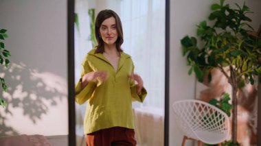 Kendine güvenen bir kadın aynada gömleğini ayarlıyor ve görünüşünü tatmin ediyor. Şık bir bayan gün ışığında kıyafet hazırlıyor. Gülümseyen esmer yansımaya hayran evde şık kıyafetlerin tadını çıkarıyor..
