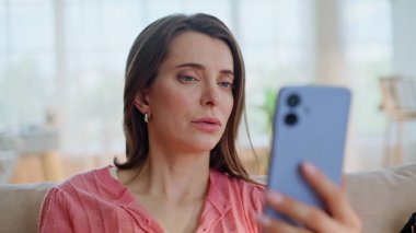 Üzgün kadın cep telefonundan rahatsız olmuş. Yakın çekimde kafaya dokunuyor. Akıllı telefondan kötü haberler okuyan üzgün bir kadın evde oturuyor. Mutsuz esmer görünümlü cep telefonu stresli..