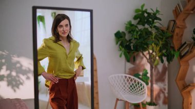 Tarz sahibi bayan, dairede şık gömlek denemekten zevk alıyor. Gülümseyen genç kadın aynaya bakıyor ve evde şık kıyafetler deniyor. Güzel esmer, oturma odasında hayranlık uyandırıyor..