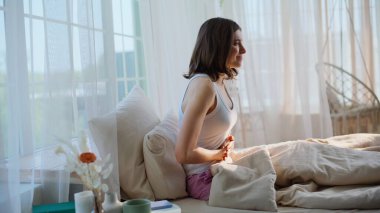 Bayan evinde rahat bir şekilde yatarken acı çeken bir dönem geçiriyor. Sabahın erken saatlerinde karın ağrısı çeken üzgün bir kadın karnına dokunuyor. Mutsuz esmer, apartman yatağında karın krampları yaşıyor..