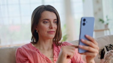 Esmer, neşeli cep telefonu mesajı rahat bir daire kanepesinde oturuyor. Cep telefonuna bakan aşırı neşeli bir kadın heyecanlı görünüyor. Finansal gelirin tadını çıkaran neşeli bayan akıllı telefon uygulaması.