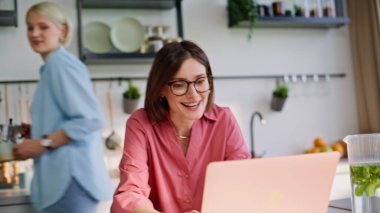 Mutlu esmer karşılama videoları mutfağa yakın çekim. Sevgi dolu kız arkadaş, espresso görünümlü bilgisayar getiriyor ve arkadaşlarına parlak mutfaktan selam veriyor. Neşeli kankalar ev içi bilgisayar kullanarak akrabalarını arıyor