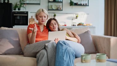 Lezbiyenler kanepede sabahları rahat rahat oturuyor. Genç lgbt çifti bilgisayar interneti kullanarak internet üzerinden tatil rezervasyonu yapmayı planlıyor. Kızlar evde rahat alışveriş yapıyor.