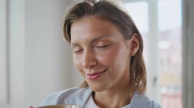 Elinde parlak oda portresiyle kahveyi tutan gülümseyen kadın. Tatmin olmuş bir kadın kameraya bakıyor ve evde sakin bir sabah geçiriyor. Neşeli kısa saç modeli. İç mekanda elinde içecek bardağıyla poz veriyor..