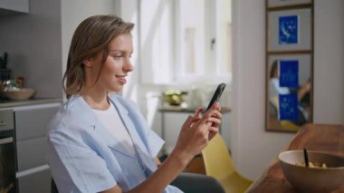 Kahvaltı sırasında cep telefonu kullanan gülümseyen bir kadın. Huzur içinde uyuyan mutlu bir öğrenci evde sosyal medyada sohbet ediyor. Pijamalı rahat bir kadın cep telefonuyla internet iletişiminin keyfini çıkarıyor..