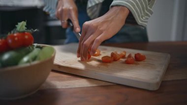 Mutfak tahtasında kiraz domatesleri kesen eller. Evde sağlıklı salata hazırlayan bir kadın taze kırmızı sebzeleri dilimliyor. Tanınmayan kadın şef organik vejetaryen yemeği pişiriyor. Aşçılık hobisi