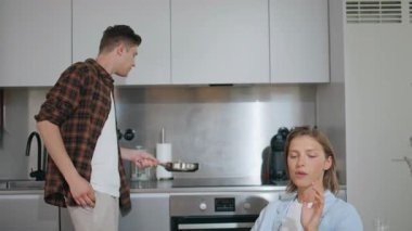 Genç erkek arkadaş sabahları yemek pişiriyor. Tasasız çift evde kahvaltı hazırlıyor. Neşeli koca, aile zamanının tadını çıkarıyor. Pijamalı, gülümseyen bir eş kocasını masada bekliyor.