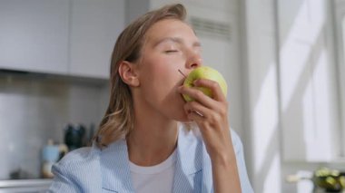 Modern bir dairede elma yiyen yakın plan kadın. Gülümseyen kız sabah yediği yeşil meyvenin tadını çıkarıyor. Neşeli kadın taze organik yemeğin tadını çıkarıyor. Sağlıklı besin konsepti.