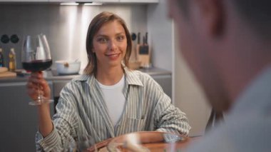 Romantik yemek sırasında kadeh kaldıran mutlu kadın. Yakın aile çifti mutfakta kırmızı şarap içiyorlar. Neşeli güzel eş hoş sohbetin tadını çıkarıyor. Eşler tarihte kutlama yapıyor.