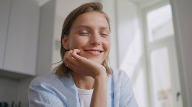 Mutlu kadın güneş ışığında dinlenen mutfağı kapatıyor. Gülümseyen ev hanımı, hafta sonları huzurlu bir sabahın tadını çıkarıyor. Evde pijamalarıyla poz veren güzel bir kız yüzü. Rahat yaşam tarzı kavramı.