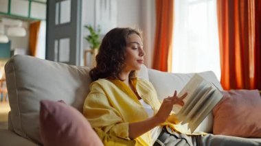 Rahat bir kadın kitap okuyor ve rahat bir şekilde kanepede oturuyor. Oturma odasında ilginç bir romanın sayfalarını çeviren genç bir bayan. Sakin kız okuyucu rahat bir dairede ev hobisinin keyfini çıkarıyor.