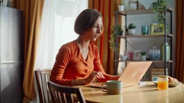 Heyecanlı bir kadın dizüstü bilgisayarını arıyor. Mutfağa yakın oturuyor. Memlekette online galibiyete duygusal tepki veren aşırı neşeli bir kadın. Mutlu esmer bayram sevinen zafer bilgisayarı. Başarı kutlamaları.