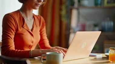 Distant employee typing computer sitting kitchen table closeup. Smart woman freelancer working laptop writing code at home. Relaxed brunette remote worker focused on screen. Online business concept.