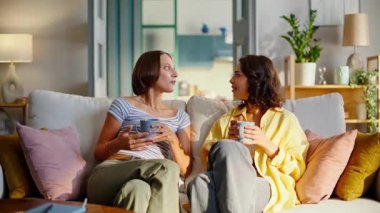Kardeşler rahat bir kanepede oturup rahatça sohbet etmeyi severler. Gülümseyen kadın arkadaşlar yurtiçi ortamda haberleri paylaşıyorlar. Pozitif kızlar ellerinde kahve fincanlarıyla kanepede dinleniyorlar..