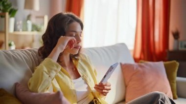 Sıkıcı kadın akıllı telefonları kaydırıyor. Ev içi hafta sonu kapanışında daire kanepesinde oturuyor. Sakin bir esmer telefon uygulaması kullanarak online alışverişleri seçiyor. Rahat bayan koltukta cep telefonuyla sosyal medyada geziniyor..