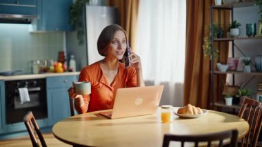 Uzaktan kumandalı bir danışman mutfak işyerinde kahve fincanını yakın çekimde oturarak akıllı telefon konuşuyor. Gülümseyen esmer serbest yazar mutfaktan cep telefonunu arıyor. Cep telefonuyla konuşan mutlu bir kadın..