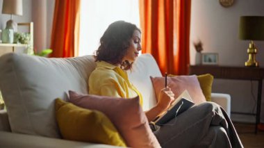 Ev hanımı, rahat bir dairede rahat rahat planlama yapıyor. Gülümseyen esmer, yaratıcı fikirlerin notlar aldığını söyleyen. Rahat kadın yazar elinde kalemle oturma odasında roman yaratıyor..