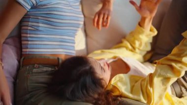 Gülümseyen kadın arkadaşının daire kanepesinde birlikte takılmasını dinliyor. Sevimli bir kız, en iyi arkadaşıyla duygusal olarak haberleri tartışıyor. Kanepede dinlenen iki genç bayan keyifli iletişimin keyfini çıkarın..