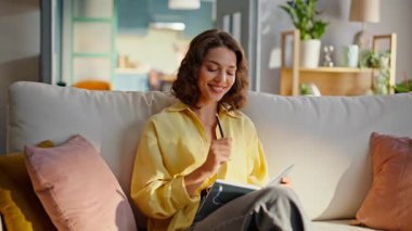 Fotokopi defterinde yazan ilham verici bir kız. Rahat bir kanepe kapanışı. Gülümseyen kıvırcık kadın yaratıcı fikirlerin notlar aldığını düşünüyor. Rahat esmer. Oturma odasında günlük tutuyor..