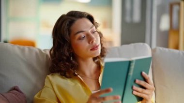 Modern apartman kanepesinde kitap okuyan yerli bir kız. Güzel kıvırcık esmer, rahat koltukta oturan ilginç bir kitapla ilgileniyor. Rahat kadın rahat evinde romantik edebiyatın tadını çıkarıyor..