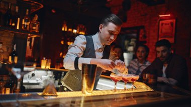 Lüks restoran tezgahında kokteylleri süsleyen barmen. Profesyonel bir bar çalışanı zarif bardaklarda alkollü içecekler hazırlıyor. Lezzetli içeceklere limon suyu ekleyen yetenekli barmen..