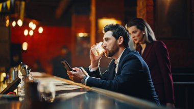 Elegant man sitting bar counter drinking cognac with smartphone alone closeup. Relaxed woman entering night restaurant start conversation with gentleman. Two people enjoying communication resting pub