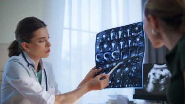 Kadın pratisyen hekim elinde x-ray ile sigorta randevusu sırasında teşhisi açıklıyor. Gülümseyen doktor, sağlık kliniğinde kadın hastayla konuşurken tıbbi tavsiye veriyor. Terapist işaret taraması