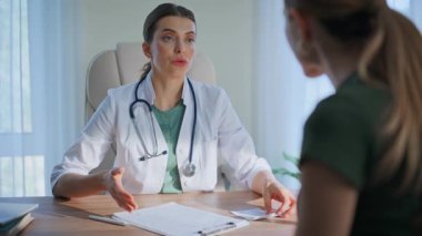 Klinik doktoru sağlık kontrolünde ilaç tavsiye ediyor. Kadın hasta ilaçlarını kontrol ediyor gülümseyerek pratisyen hekimi ziyaret ediyor. Randevu sırasında sağlık uzmanı danışmanlık hizmeti sunar