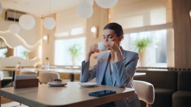 Kahve içen zarif bir bayan restoran masasına yakın çekim yapıyor. Kendine güvenen iş kadını, rahat kafeteryada tek başına dinleniyor. Modern kafede dinlenen rahat bir kadın sıcak içeceğin tadını çıkarıyor. Boş zaman kavramı