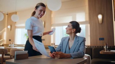 Çağdaş restoranda kahve molasında cep telefonuna mesaj atan gülümseyen bayan patron. Kafedeki telefon mesajlarını okuyan mutlu bir iş kadını. Dost canlısı garson kız müşteriden sipariş alıyor.