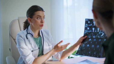 Klinikte röntgen çektiren bir doktora danışıyorum. Muayene sırasında gülümseyen tıbbi uzman teşhisi açıkladı. Taramaları inceleyen pratisyen kadın, modern sağlık hizmetleri ofisinde sonuç veriyor.