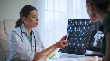 Sağlık uzmanı, endişeli hastalarla tıbbi tavsiyeler hakkında konuşmak için röntgen çekiyor. Dost canlısı doktor özenli kadına sağlık bilgilerini açıklıyor. Klinikte kemik taraması yapan sıhhiye kadın.