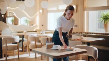 Cafe garsonu, müşterilerden sonra bulaşıkları yıkıyor. Lokanta temizliğinde çalışan kız çalışanlar. Rahat kadın konukseverlik ortamında temizliği sağlamak için bardakları tepsiye koyuyor.