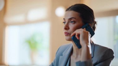 Dinlenmiş esmer konuşan cep telefonu modern kafede kruvasan yiyor. Akıllı telefondan konuşan çekici genç bir kadın küçük restoran masasında oturuyor. Çevrimiçi kadın akıllı telefon konuşması yapıyor.