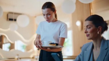 Cep telefonlu sosyal medya izleyen odaklanmış iş kadını rahat kafeteryayı tek başına kapatıyor. Gülümseyen kadın garson müşteriye tatlı servisi yapıyor. Cafe molasında dinlenen zarif bir bayan.