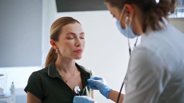 Doktor hanım sağlık kontrolü sırasında steteskop kullanıyor. Hasta kadın kliniği ziyaret ediyor. Odaklanmış sağlık çalışanı, kadın hastaya teşhis konusunda vücut danışmanlığı yapıyor. Genel profesyonel konuşma hasta kız