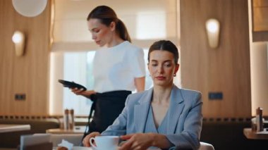 Cafe müşterisi yemeğini bitiriyor. Akıllı telefonuyla nakit ödeme yapıyor. Dost canlısı bayan garson, alışveriş için iş kadınına terminali veriyor. NFC teknolojisinden restoran faturası ödeyen bayan.