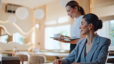 Kendine güveni tam bir iş kadını. Akıllı telefona benziyor. Lokantada kahvesini bekliyor. Konforlu kafeteryada garson kız müşteriye servis yapıyor. Rahat bir kadın modern kafede tek başına cep telefonu kullanıyor.