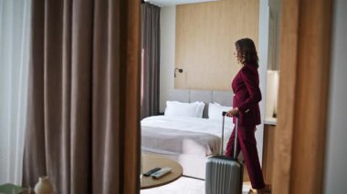 Lüks otele gelen iş kadını. Gülümseyen zarif bir kadın rahat bir yatak odasına modern bir şekilde giriyor. Dairede bavul taşıyan kendine güvenen mutlu bir bayan. İş gezisi.