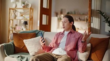 Hafif oturma odasında akıllı telefondan modern etkiye sahip biri var. Esmer adam cep telefonu ekranına el hareketi yapıyor. Rahat olumlu adam blogcusu koltuktaki cep telefonunda video içeriği kaydediyor