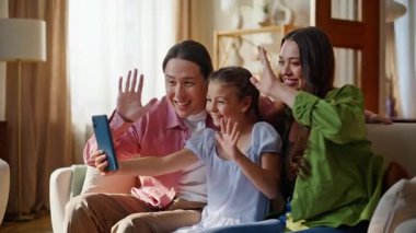 Neşeli akrabalar evdeki akıllı telefonları arıyor. Olumlu anne-baba ve kızı internette el sallayarak sohbet ediyorlar. Cep telefonuna gülümseyen aile selamlaması