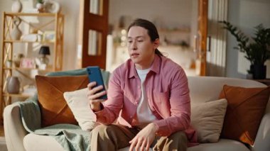 Asyalı bir öğrenci akıllı telefondan kameralı sohbet ederek kanepeye yakın çekim yapıyor. Evde cep telefonuyla haberleri tartışan yakışıklı bir adam. Olumlu gülümseyen adam cep telefonuyla çevrimiçi konuşma yapıyor.