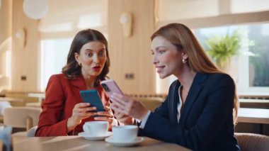 Neşeli arkadaşlar cep telefonu haberlerini sıcak kafeteryaları kapayarak paylaşıyorlar. İki kadın akıllı telefonları izlerken gülümsüyor ve birlikte başarıyı kutluyorlar. Neşeli iş ortakları cep telefonu mesajı okuyor.